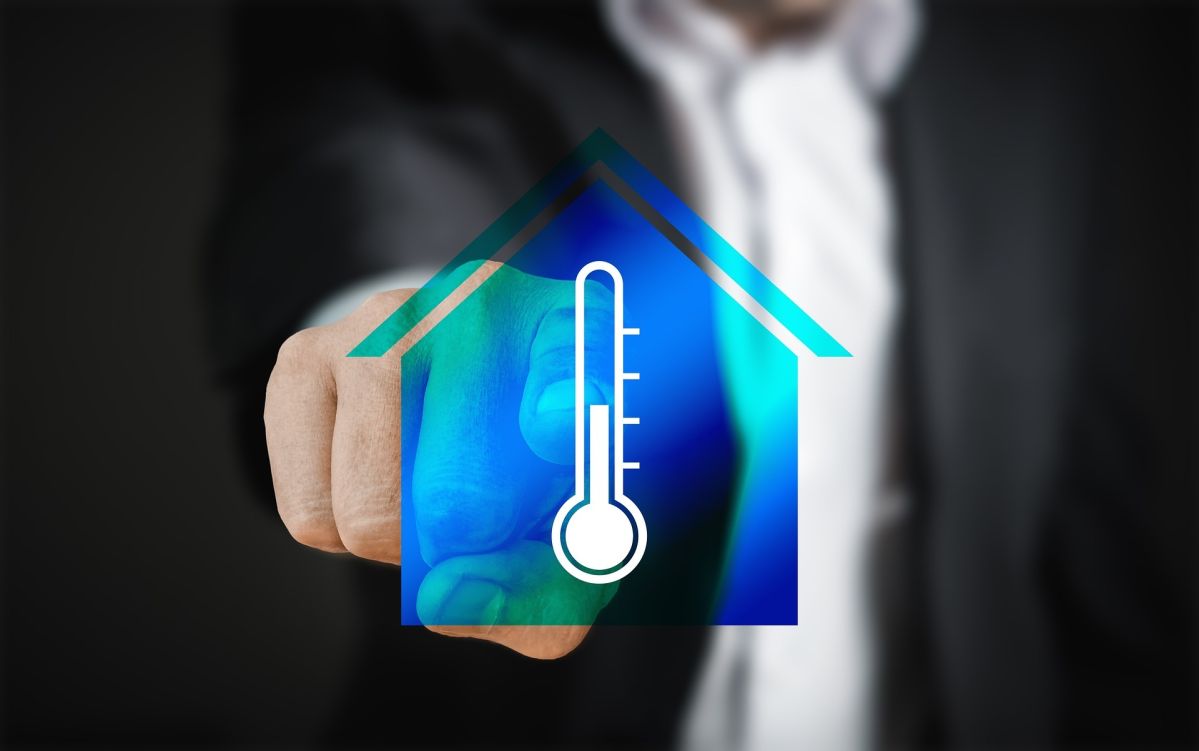 Eine Hand zeigt auf ein transparentes, blaues Haus-Symbol mit einem Thermometer darauf, das in einem dunklen, unbestimmten Umfeld schwebt.