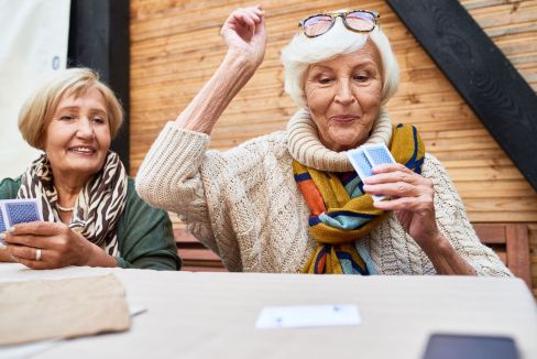 2 ältere. fröhliche Frauen sitzen an einem Tisch und spielen mit Karten.