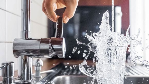 Eine Person füllt eine Wasserglas mit Schwung an einem Wasserhahn in einer Küche.