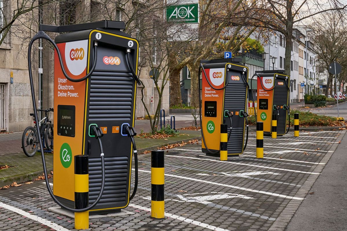 Drei Ladesäulen der evm in Orange und Schwarz auf leeren Parkplätzen mit E-Auto-Symbol