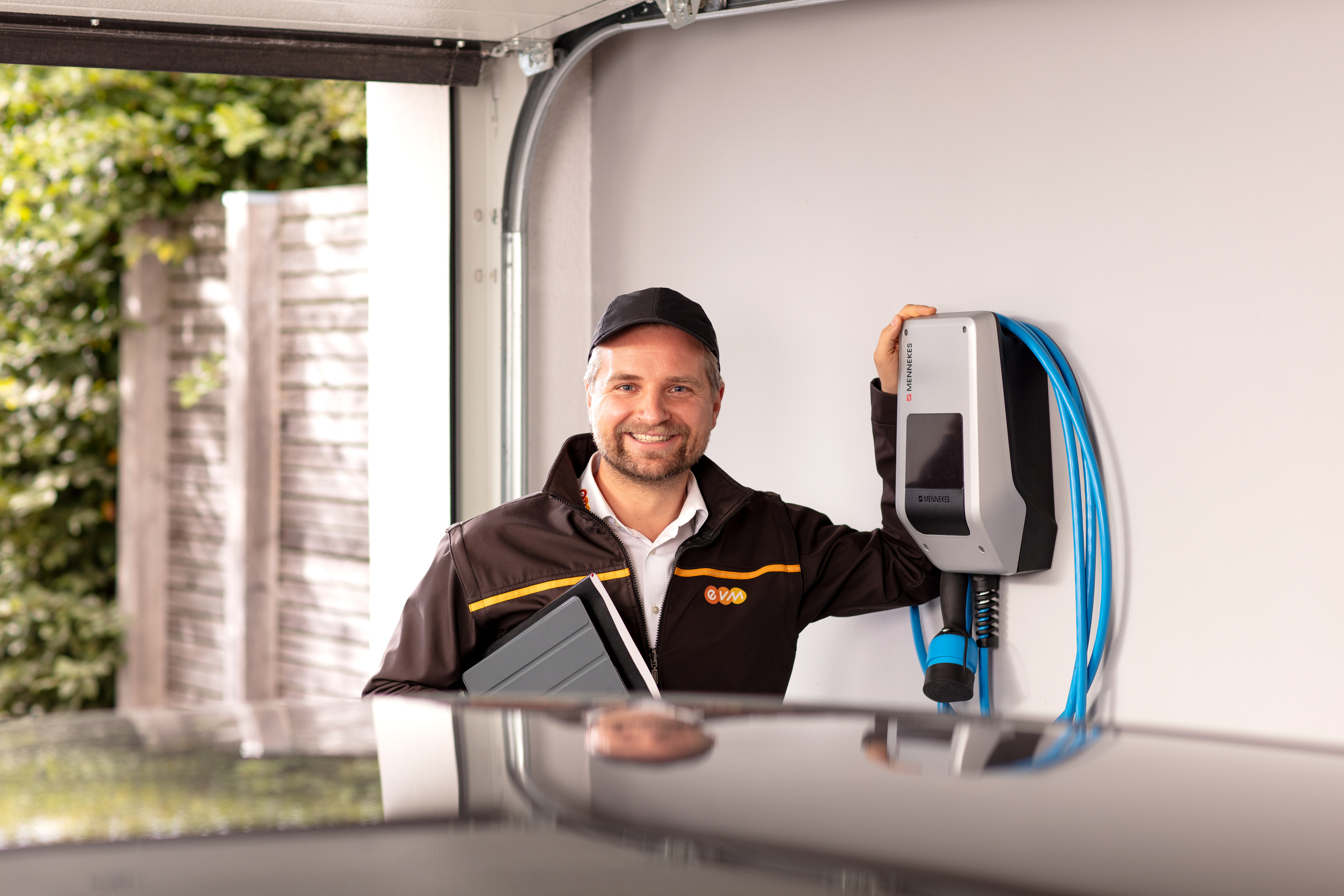 Ein Monteur der evm lehnt an einer Wallbox und lacht in die Kamera