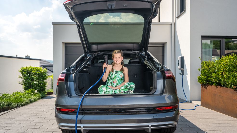 Ein Mädchen sitzt im Kofferraum eines E-Autos und hält ein blaues Ladekabel.