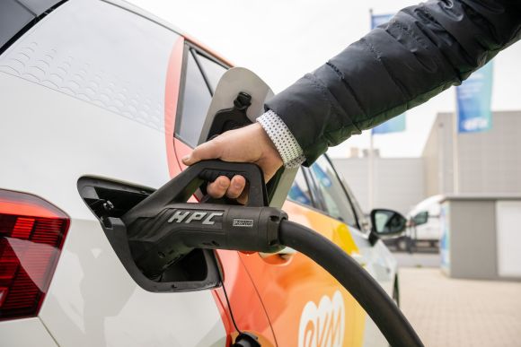 Eine Person lädt ein orangenes evm E-Auto mit einem schwarzen Ladekabel.