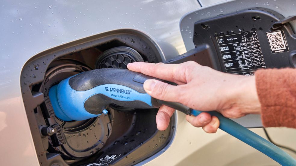 Eine Person lädt ein E-Auto mit einem blauen Ladekabel.