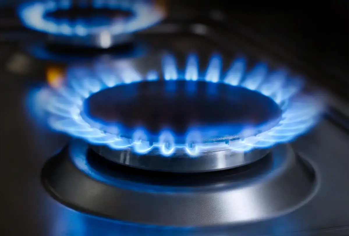 Ein Gasherd brennt, mit blauen Flammen, die gleichmäßig um den runden Brenner verteilt sind, in einer modernen Küche. Ein weiterer Brenner ist unscharf im Hintergrund sichtbar.