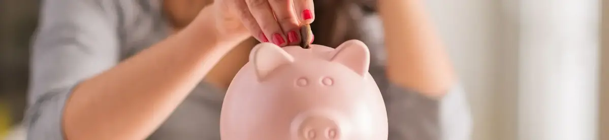 Eine rosafarbene Sparbüchse, Münze einwerfend, von einer Hand mit roten Fingernägeln; unscharfer Hintergrund mit Person in gestreiftem Hemd.