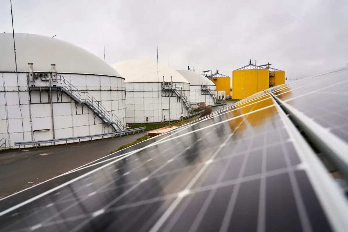191206SDI1044 Im Vordergrund ist eine dunkle PV-Anlage zu erkennen. Links i Hintergrund befinden sich große weiße und gelbe Kessel.