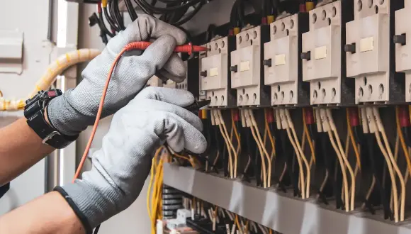 Eine Person mit Arbeitshandschuhen arbeitet an einem Stromkasten.