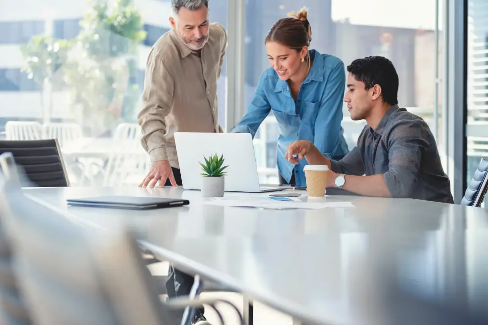 Group of business people working Zwei professionell gekleidete Männer und eine Frau sitzen an einem Besprechungstisch. Sie schauen auf einen Laptop und diskutieren.