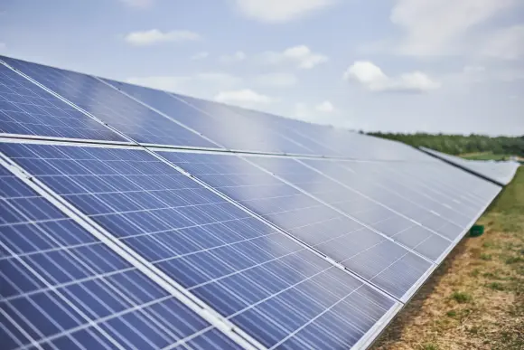 Himmelblick auf einen Solarpark in einer begrünten Umgebung und blauem Himmel mit weißen Wolken.
