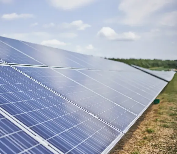 Himmelblick auf einen Solarpark in einer begrünten Umgebung und blauem Himmel mit weißen Wolken.