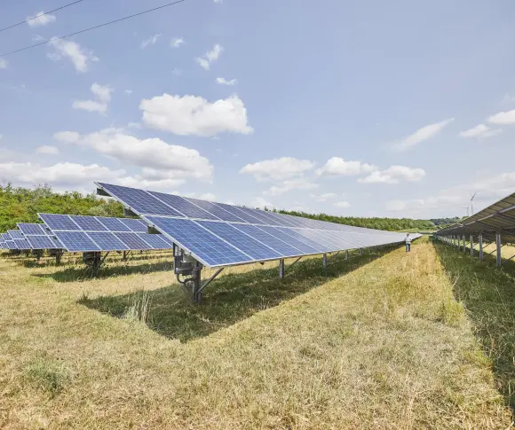 Himmelblick auf einen Solarpark in einer begrünten Umgebung und blauem Himmel mit weißen Wolken.