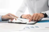 Business people negotiating a contract. Zwei Personen sitzen an einem Besprechungstisch. Vor ihnen liegt ein Clipboard auf dass sie zeigen.