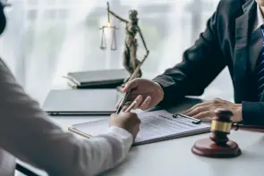 Hammer, judge, lawyer, businessman, scales, god of justice, laptop notebook on table, legal advisor concept Judge with justice lawyers having team meeting at office background Eine Person unterschreibt ein Dokument auf einem Tisch. Ein Richterhammer und eine Justitia-Statue befinden sich daneben in einem Büro oder Konferenzraum.