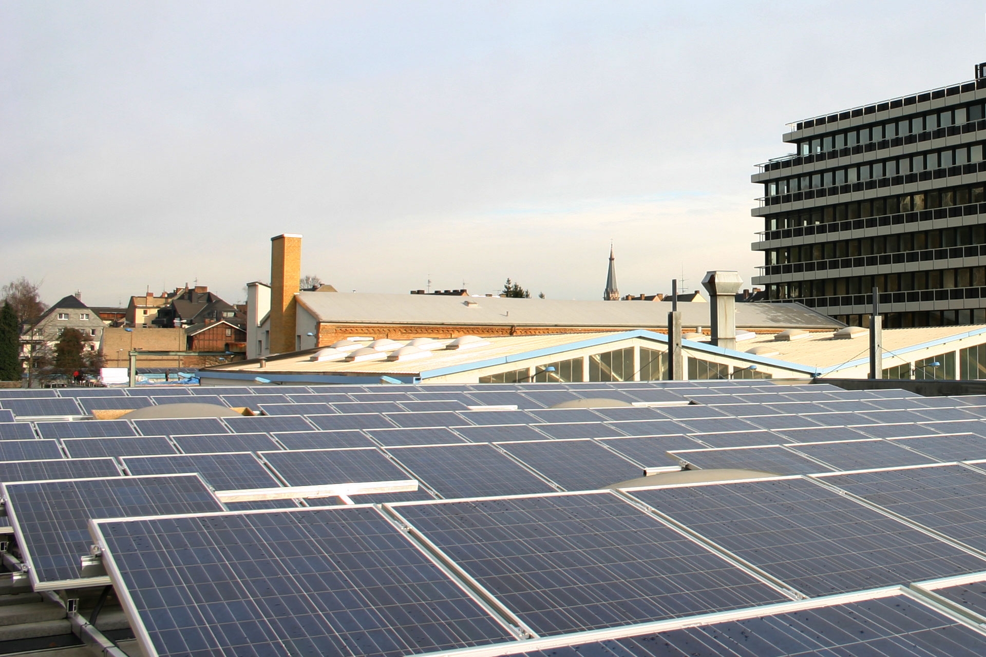 Im Vordergrund sind viele PV-Panele auf einem Firmendach, im Hintergrund mehrere Gewerbegebäude
