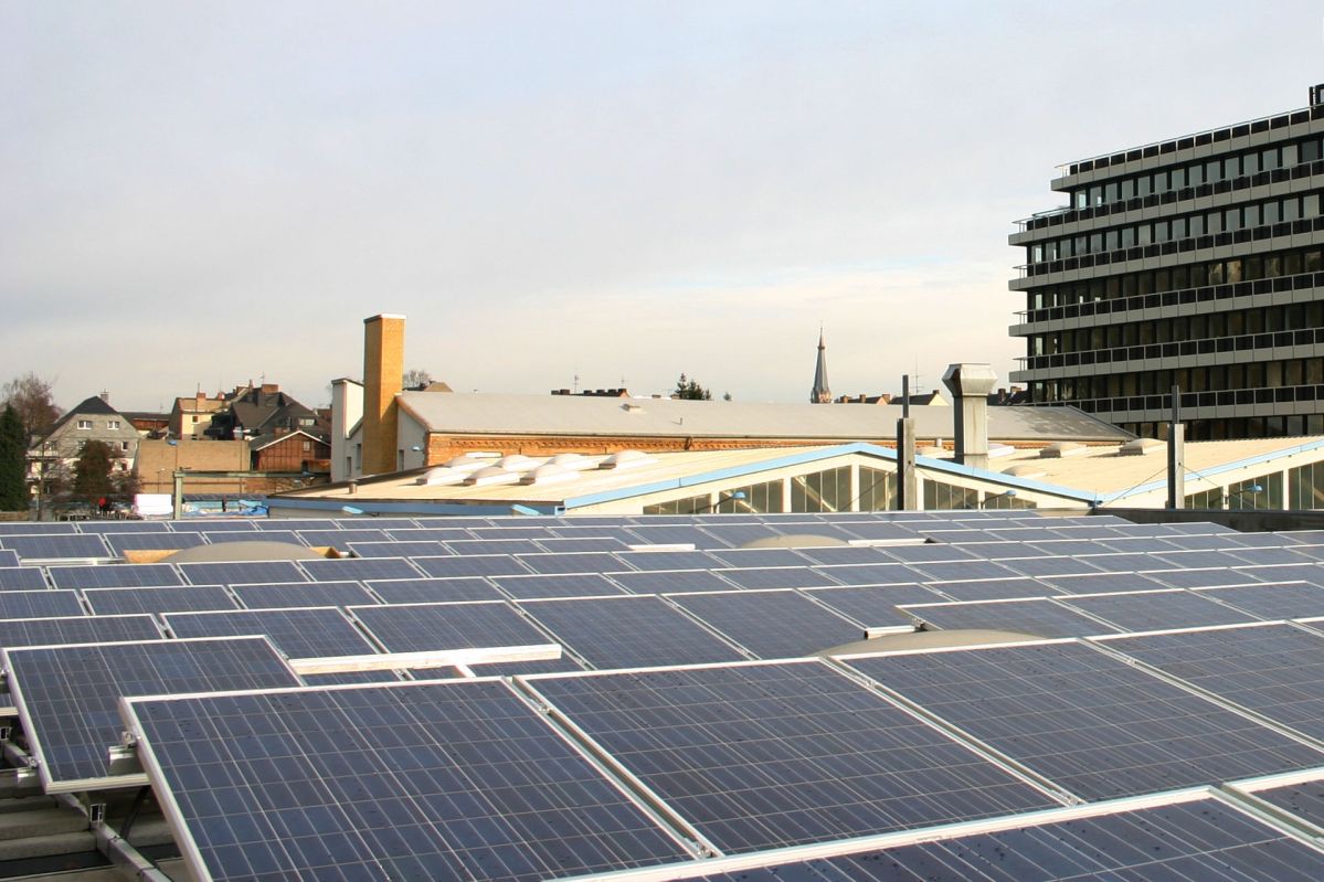 Im Vordergrund sind viele PV-Panele auf einem Firmendach, im Hintergrund mehrere Gewerbegebäude