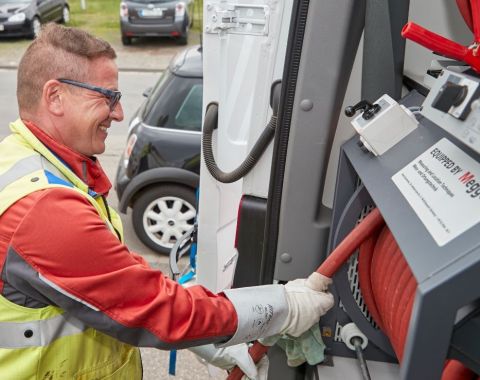 Ein Mann in Arbeitskleidung stellt etwas ein an einem Kabelmesswagen. Er lacht freundlich und trägt eine Schutzbrille.