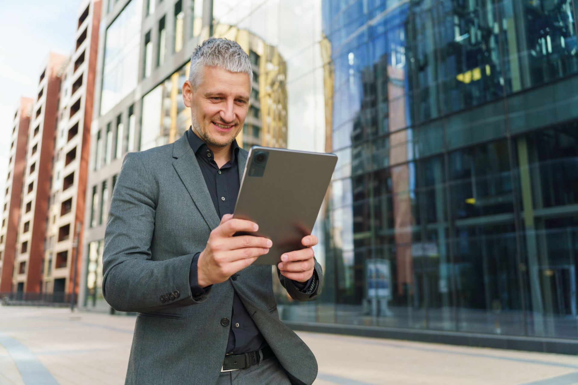 Lieferantenwechsel in 24 Stunden – Das ändert sich 2025 A businessman in a gray suit stands outside a modern building, focused on using a tablet device.
