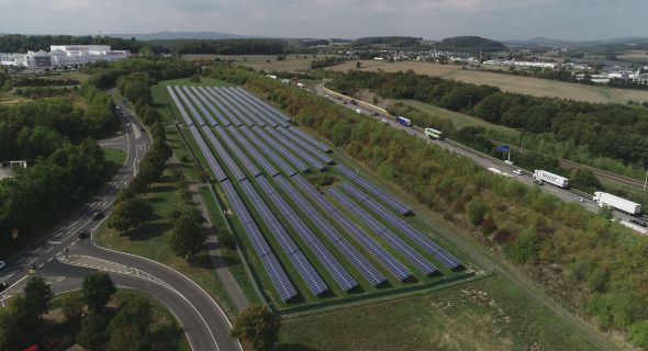 Himmelblick auf einen Solarpark in einer begrünten Umgebung und blauem Himmel mit weißen Wolken.