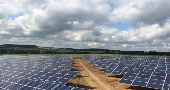 Himmelblick auf einen Solarpark in einer begrünten Umgebung und blauem Himmel mit weißen Wolken.