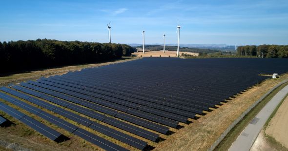 Himmelblick auf einen Solarpark in einer begrünten Umgebung und blauem Himmel mit weißen Wolken.