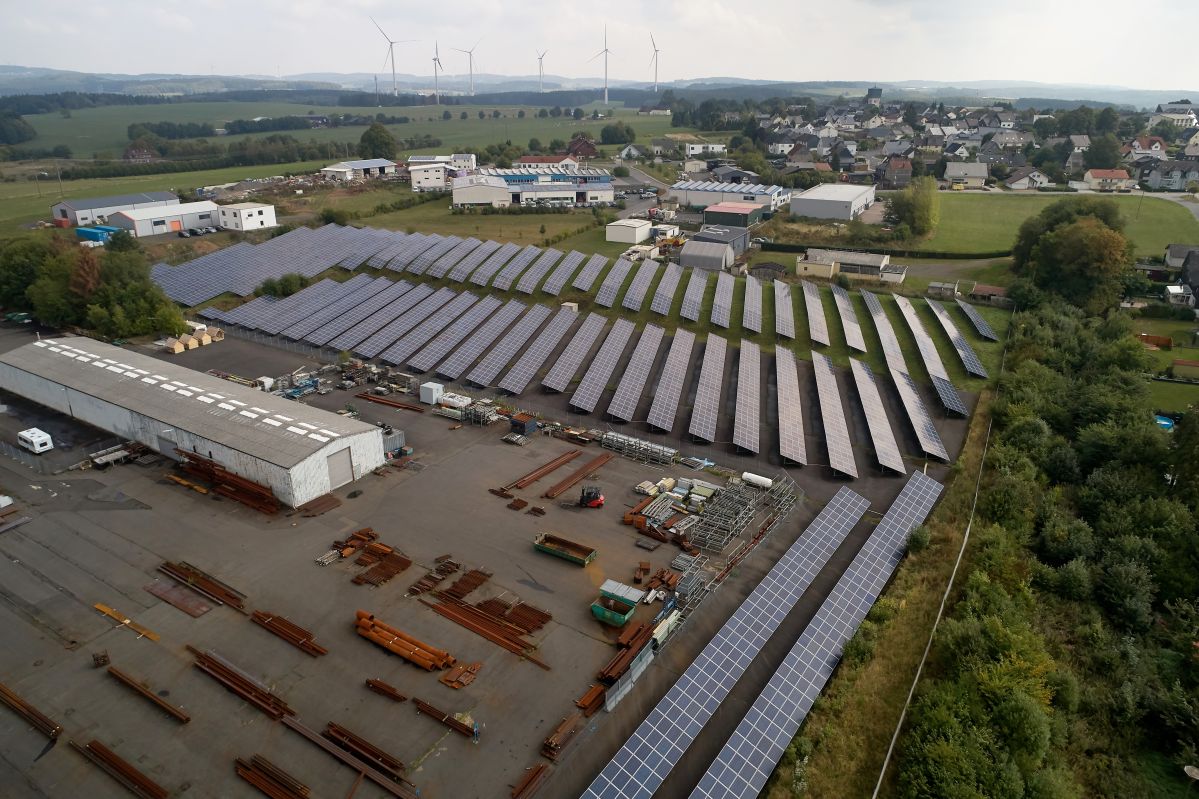 EVM-Solarpark Höhn Himmelblick auf einen Solarpark in einer begrünten, bewohnten Umgebung. Daneben eine große Lagerhalle.