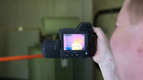 En Mann hält eine Thermografie Kamera und führt eine Elektro-Thermografie Messung durch.