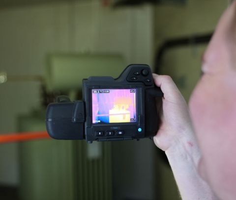 En Mann hält eine Thermografie Kamera und führt eine Elektro-Thermografie Messung durch.