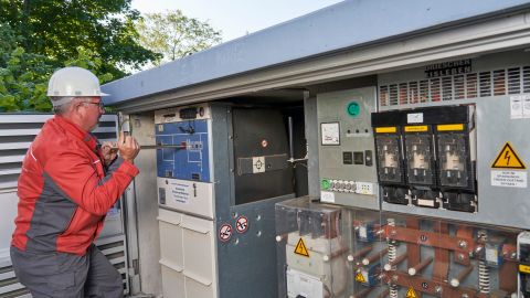 Ein Mann in roter Arbeitskleidung und Schutzhelm arbeitet an einer Transformatorenstation.