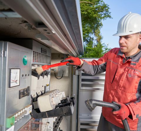 Ein Mann in roter Arbeitskleidung und Schutzhelm arbeitet an einer Transformatorenstation.