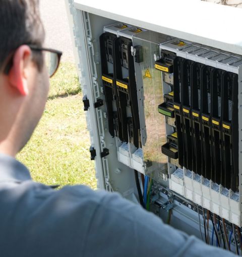 Ein Mann mit grauem Poloshirt und Brille arbeitet an einem Stromkasten.