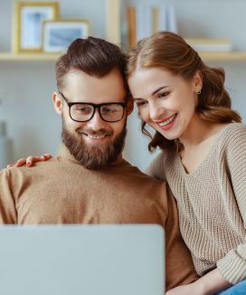 Mann und Frau vor Laptop Ein Mann und eine Frau sitzen vor einem Laptop und lächeln freundlich.
