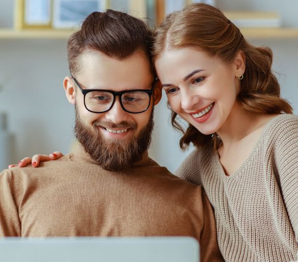 Mann und Frau vor Laptop Ein Mann und eine Frau sitzen vor einem Laptop und lächeln freundlich.