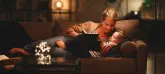 Eine Frau liegt mit ihrer Tochter auf einem Sofa und liest aus einem Buch vor. Auf dem Sofatisch steht ein Glas mit einer Lichterkette.