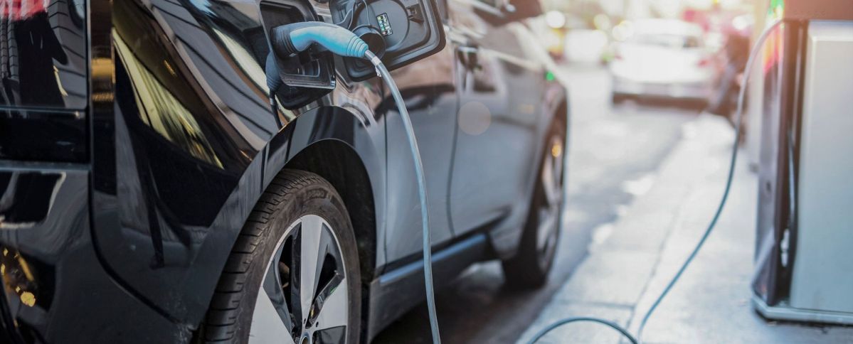 Elektroauto am laden Ein schwarzes Elektroauto wird auf einer städtischen Straße über ein blaues Ladekabel aufgeladen. Im Hintergrund sind verschwommene Autos und Gebäude sichtbar.