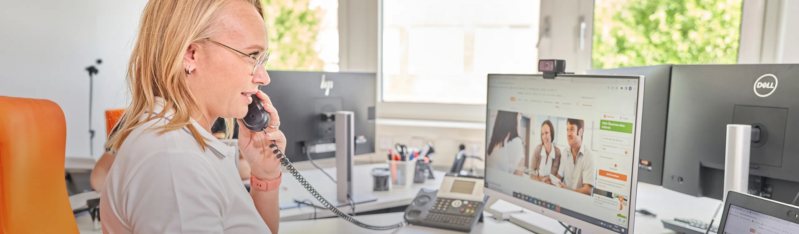 Eine Person telefoniert an einem Schreibtisch, während sie auf einen Monitor schaut, der eine evm-Webseite zeigt. Im Hintergrund befinden sich Fenster und Büroutensilien.