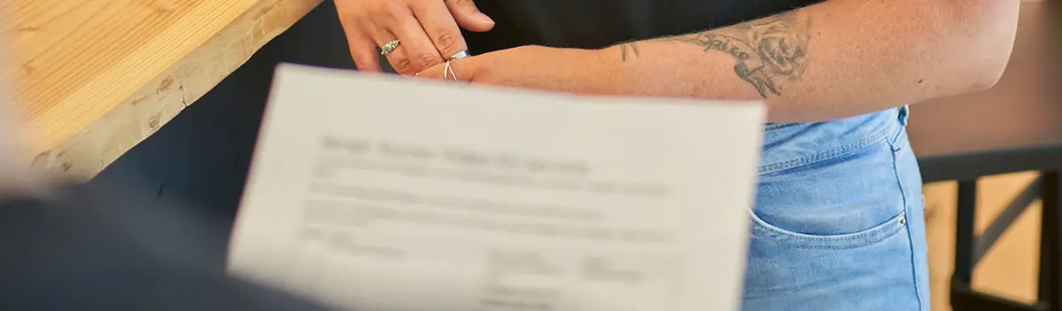 Eine Person hält eine Rechnung die verschwommen ist. Im Hintergrund ist der Arm einer Frau erkennbar.