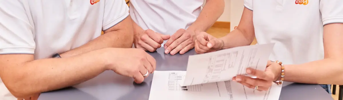 Drei Personen in weißen evm T-Shirts stehen um einen Tisch und schauen auf Unterlagen.