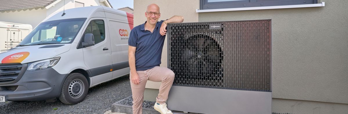 Wärmepumpe im Praxistest Thomas Schmitz steht neben einer außen installierten Wärmepumpe, die vor der Hauswand montiert ist. Im Hintergrund ist ein weißer Transporter mit „ewm“-Logo zu sehen.