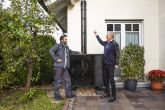 Ein Mann und ein evm Mitarbeiter stehen in einem Garten vor einer Wärmepumpe. Der Mann zeigt auf etwas während der Arbeiter an der Wärmepumpe lehnt.