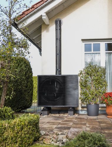 Das Außenelement einer Wärmepumpe vor einem Altbau.