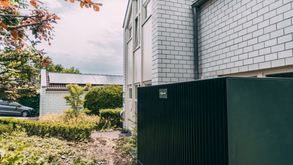 Eine Wärmepumpe steht vor einem weißen Haus in einer grünen Umgebung.