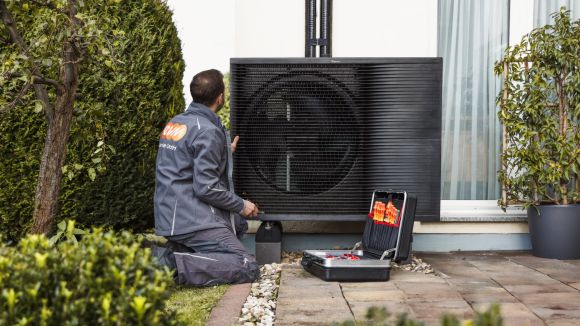 Ein Mann mit evm Service GmbH Arbeitskleidung kniet vor einer Wärmepumpe. Neben ihm steht ein Werkzeugkasten.