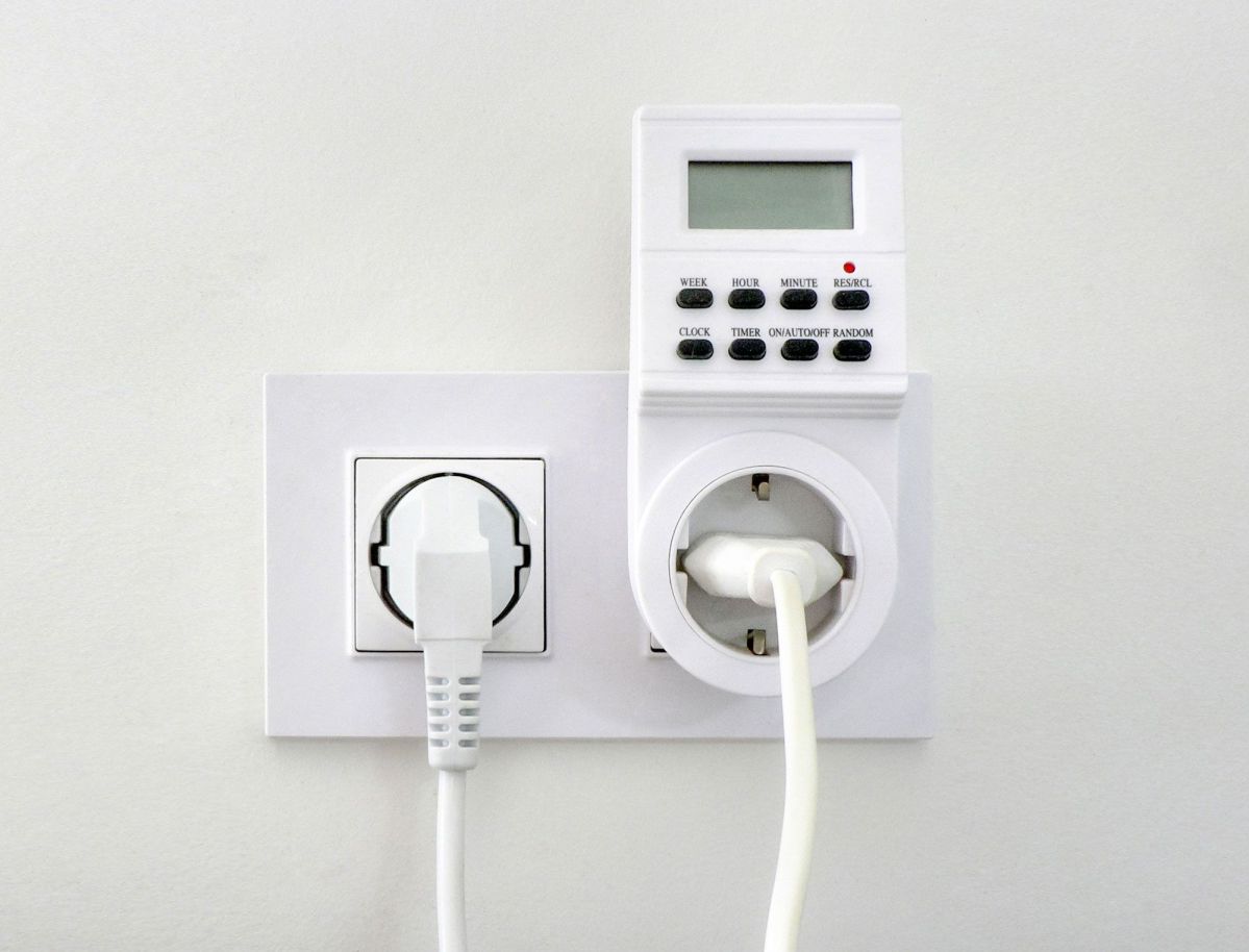 evm Heizung Regulator Eine Zeitschaltuhr ist in eine Steckdose eingesteckt, mit einem daran angeschlossenen Kabel. Der Hintergrund ist eine weiße Wand.