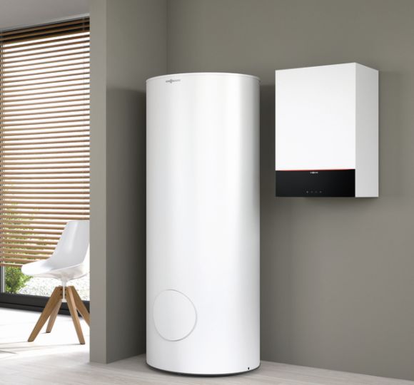 Eine große, weiße Hybridheizung steht neben einem kleinen Wandgerät in einem modernen, minimalistisch eingerichteten Raum.