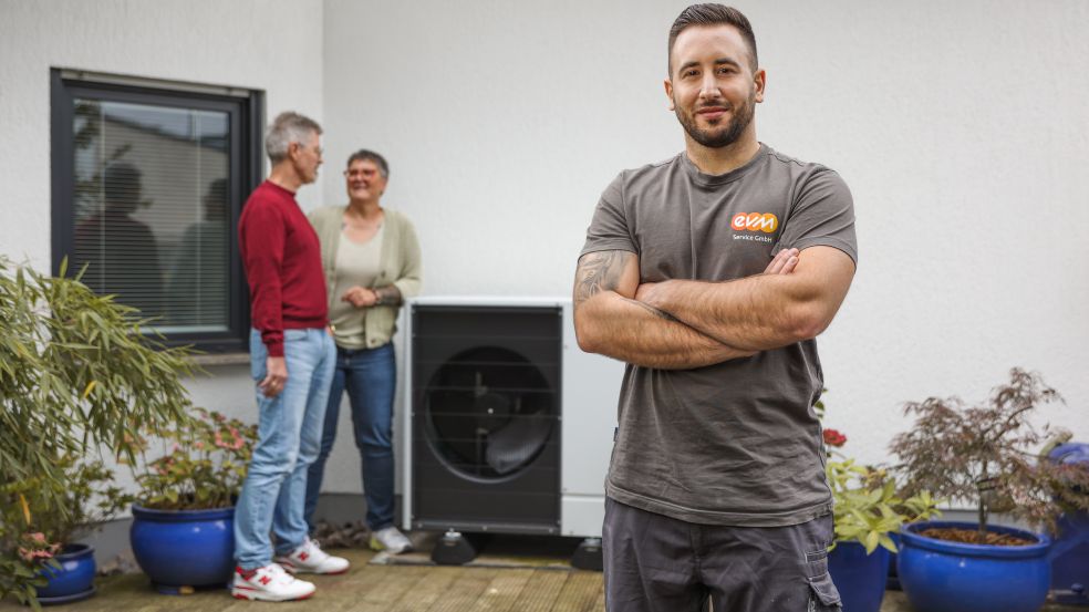 Eine Monteur im Vordergrund, eine Familie vor ihrer Wärmepumpe im Hintergrund