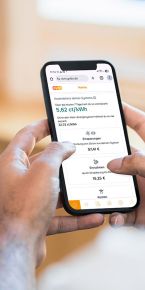 Eine Person hält ein Smartphone in beiden Händen und betrachtet in der evm‑App Energieinformationen wie Kosten, Einsparungen und Erträge auf einem hellen, unscharfen Hintergrund.