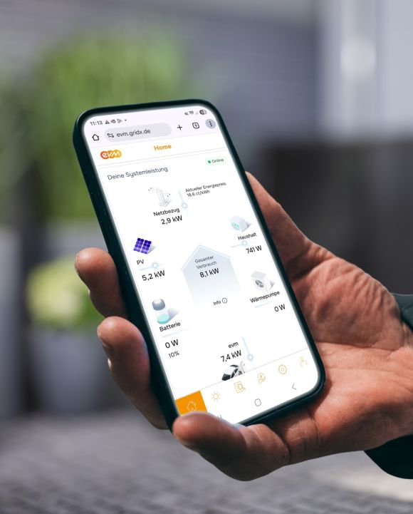 Eine Person hält ein Smartphone in der Hand und betrachtet in der evm⁺ App die aktuelle Energieübersicht mit Angaben zu Stromerzeugung, Verbrauch und Speicherstatus.