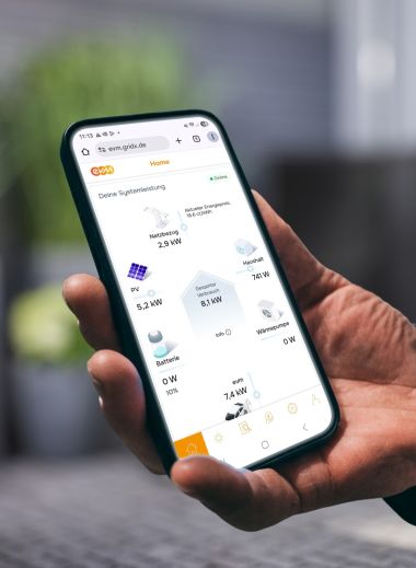 Eine Person hält ein Smartphone in der Hand und betrachtet in der evm⁺ App die aktuelle Energieübersicht mit Angaben zu Stromerzeugung, Verbrauch und Speicherstatus.