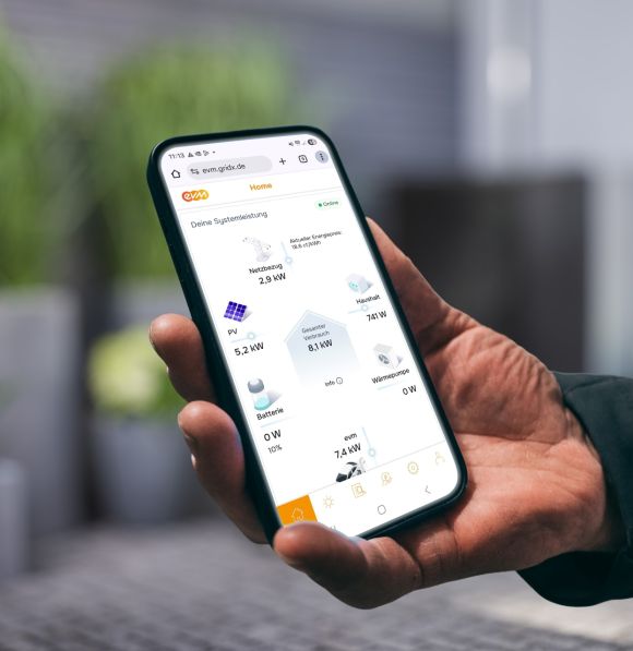 Eine Person hält ein Smartphone in der Hand und betrachtet in der evm⁺ App die aktuelle Energieübersicht mit Angaben zu Stromerzeugung, Verbrauch und Speicherstatus.